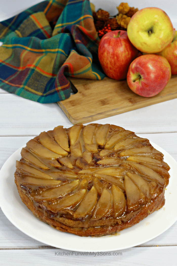 A cinnamon roll apple upside down cake on a white serving platter with apples in the background