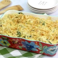 A floral baking dish filled with chicken spaghetti casserole sitting on a green plaid napkin
