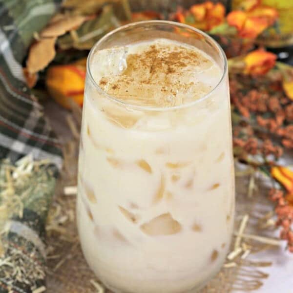 A pumpkin white Russian in a tall glass with fall decorations in the background