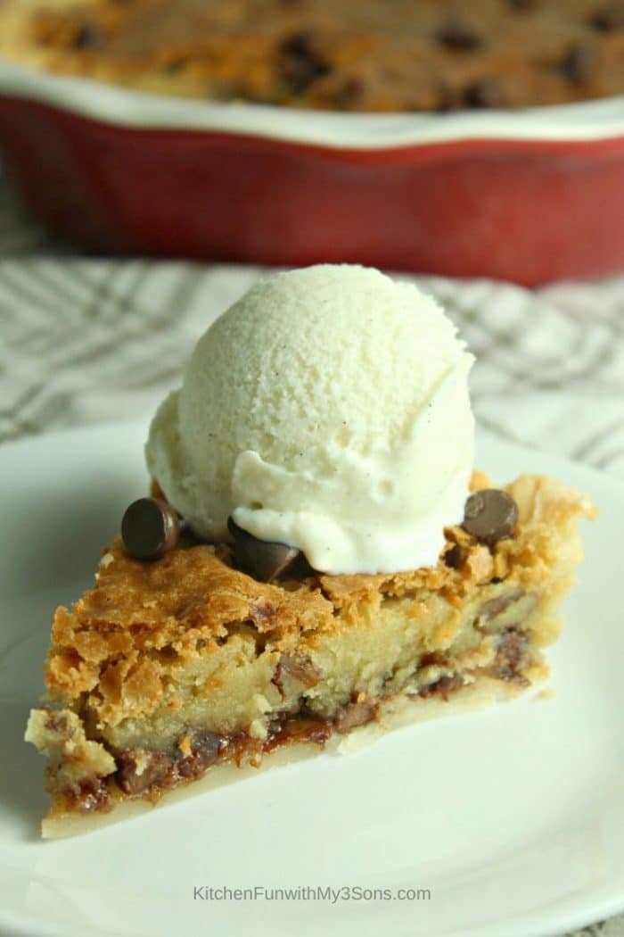 A single slice of chocolate chip pie on a white saucer with ice cream on top
