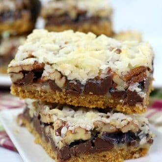 A stack of hello dolly bars on a white plate topped with coconut