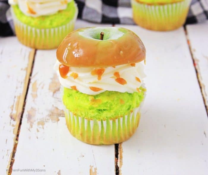Apple cupcakes with caramel apple on top sitting on a wooden surface with black plaid cloth in background