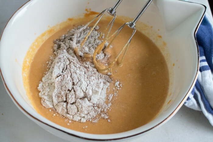 Adding flour to the bowl of pumpkin pie batter.
