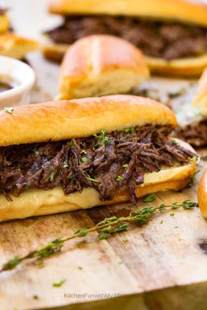 French dip sandwiches ready to eat and laying on a wooden cutting board