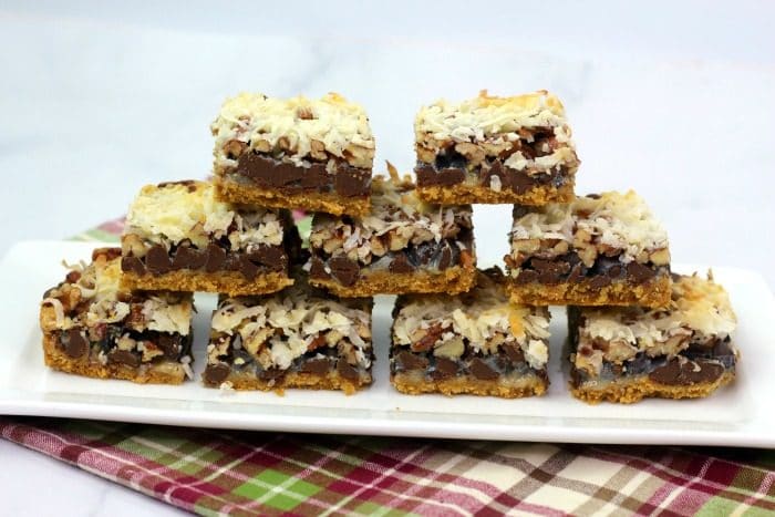 Hello Dolly Cookie Bars in a pyramid stack on a white serving tray on red plaid cloth