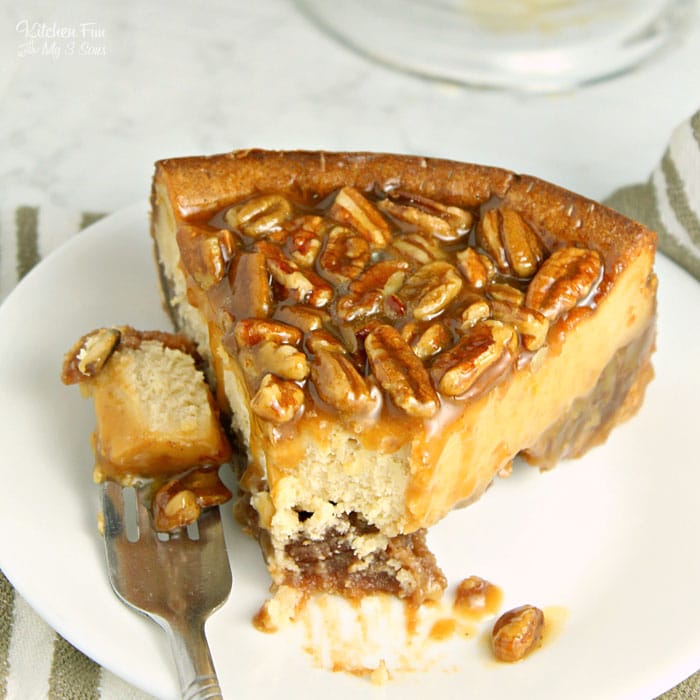 Overhead shot of a slice of pecan pie cheesecake on a white platter. A forkful of cheesecake has been cut from the slice and is lying on the plate.