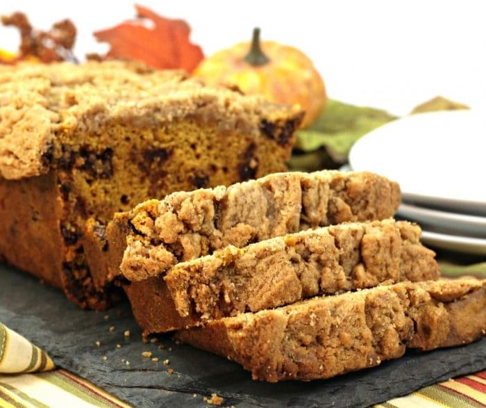 Slices of pumpkin streusel bread with chcoolate chips laying on a gray cloth with fall decor in background