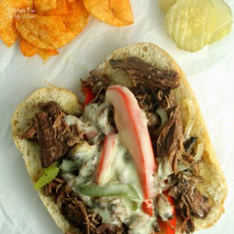 Overhead view of an open-faced slow cooker drip beef sandwich next to potato chips.