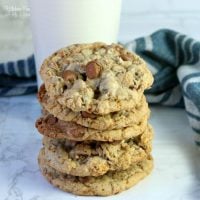 A stack of toffee chocolate chip cookies next to a glass of milk.