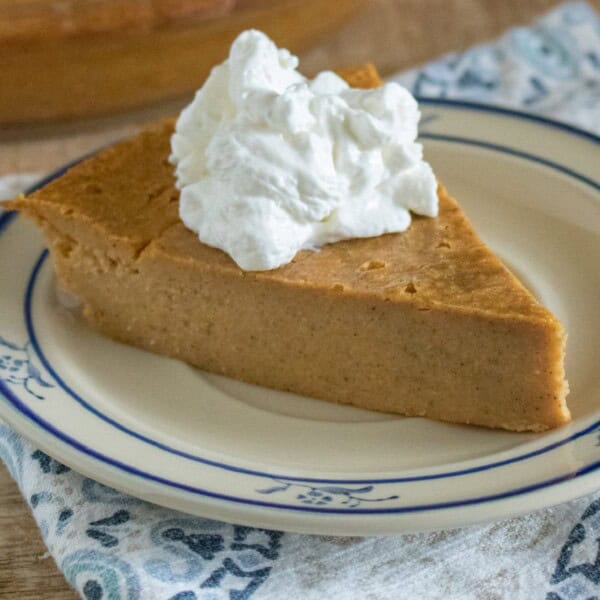 Close up view of a slice of Crustless Pumpkin Pie topped with whipped cream on a plate.