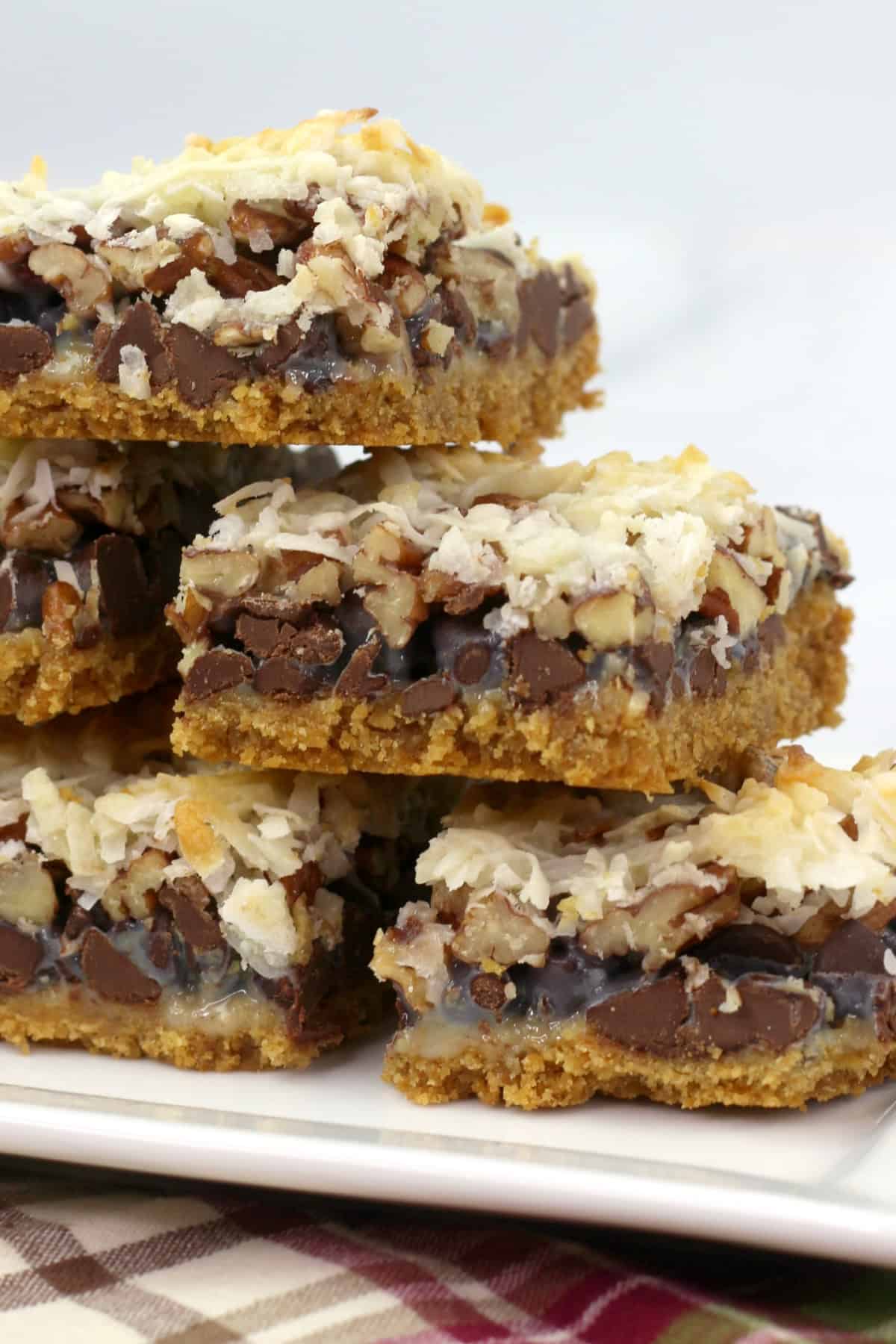 These Hello Dolly Bars are loaded with chocolate chips, coconut, and crunchy pecans over a buttery graham cracker crust. Hello Dolly Bars stacked on a platter