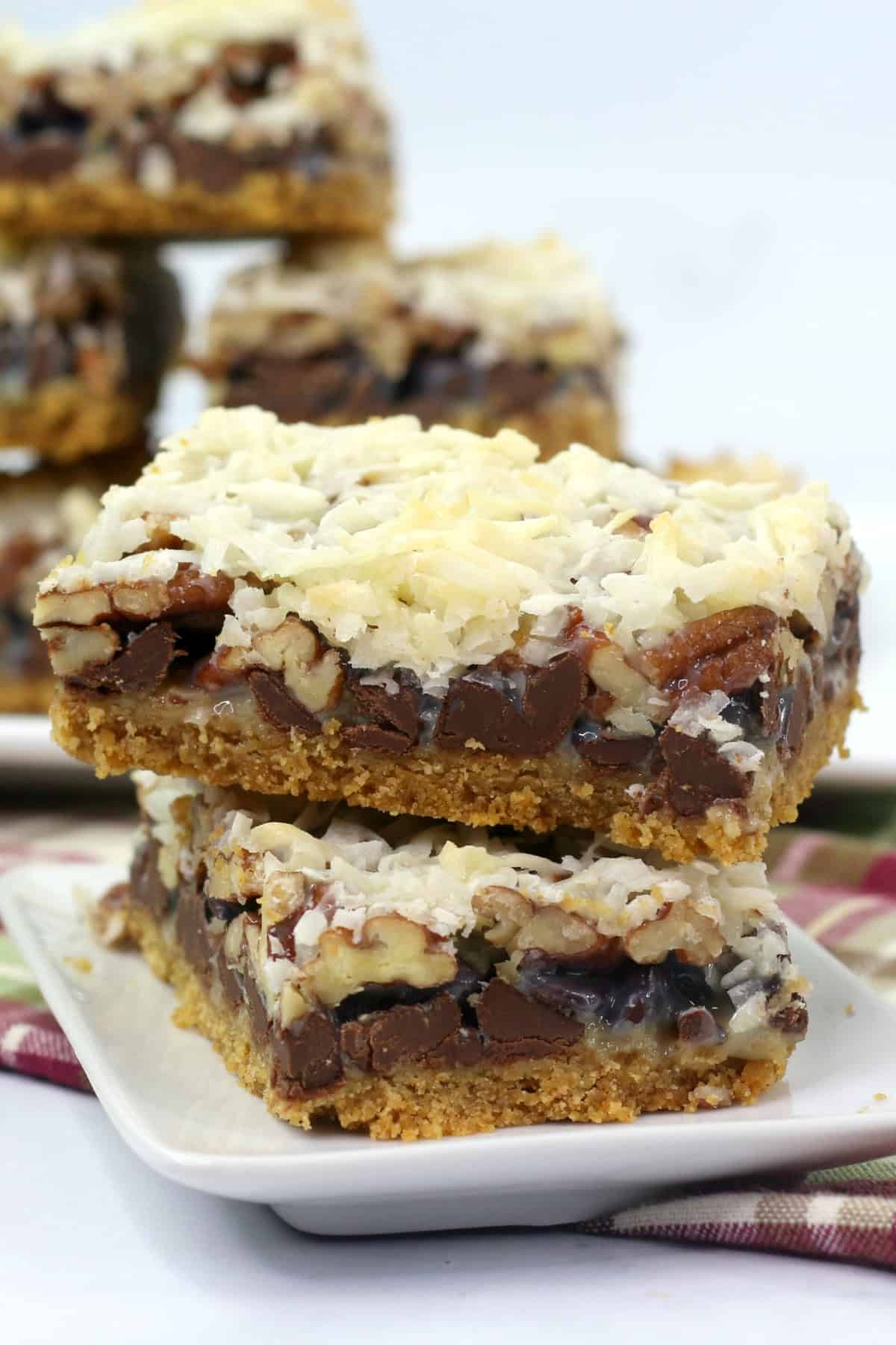 These Hello Dolly Bars are loaded with chocolate chips, coconut, and crunchy pecans over a buttery graham cracker crust. Hello Dolly Bars stacked on a plate.