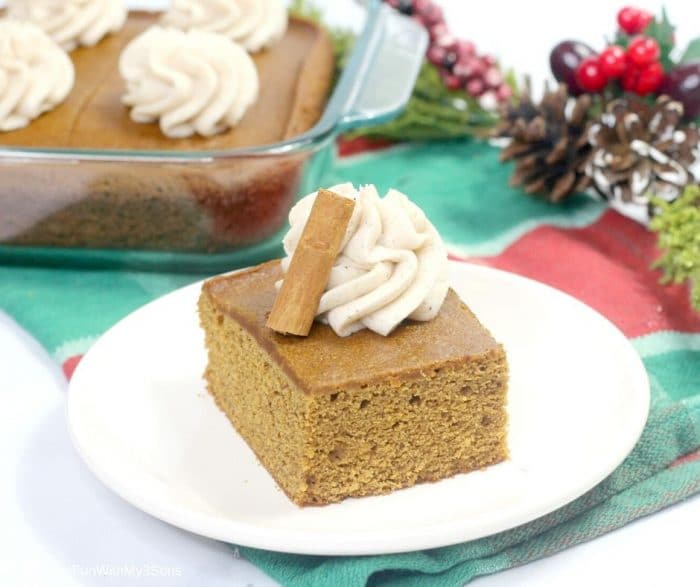 A slice of gingerbread cake on a white plate with holiday decor in the background