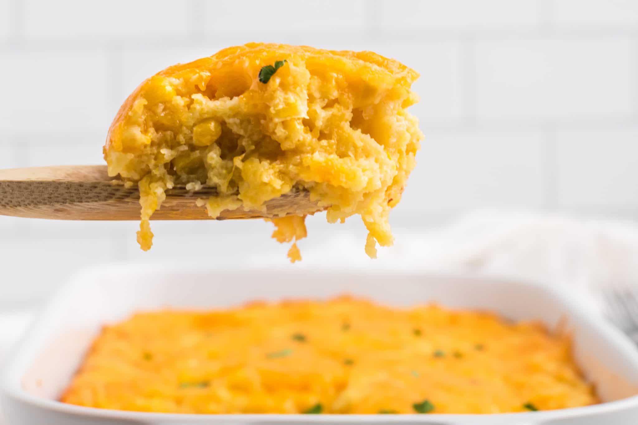 A wooden spoon holding a serving of cheesy corn casserole