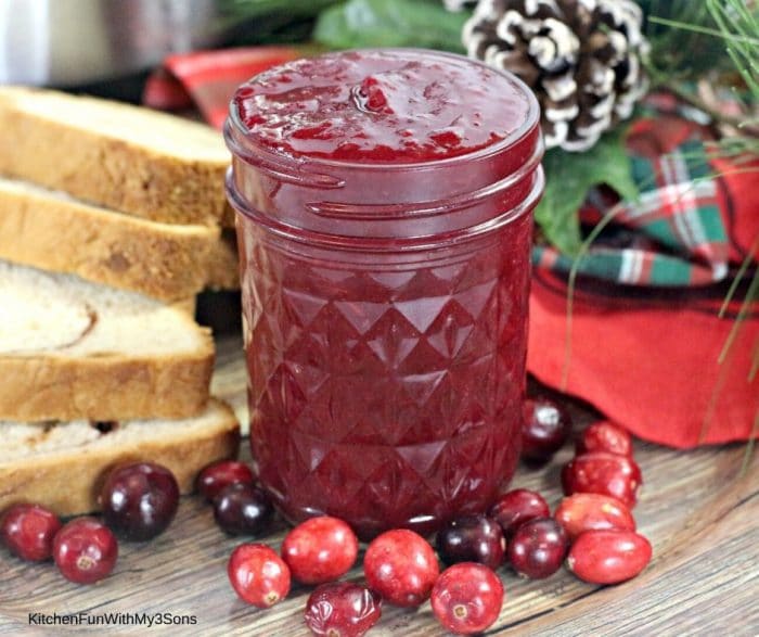 Sliced bread next to a jar of cranberry butter with fresh cranberries on the table
