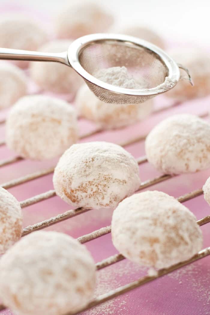 Dusting powdered sugar over cookies on a cooling rack