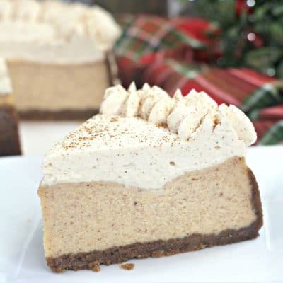 Up close picture of a slice of eggnog cheesecake on a plate in front of holiday decor