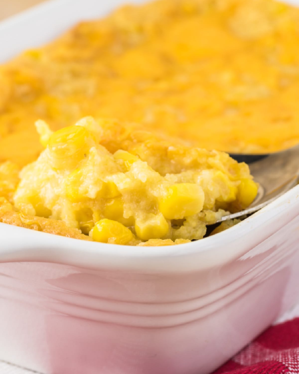 Cheesy Corn Casserole being lifted out of a glass baking dish