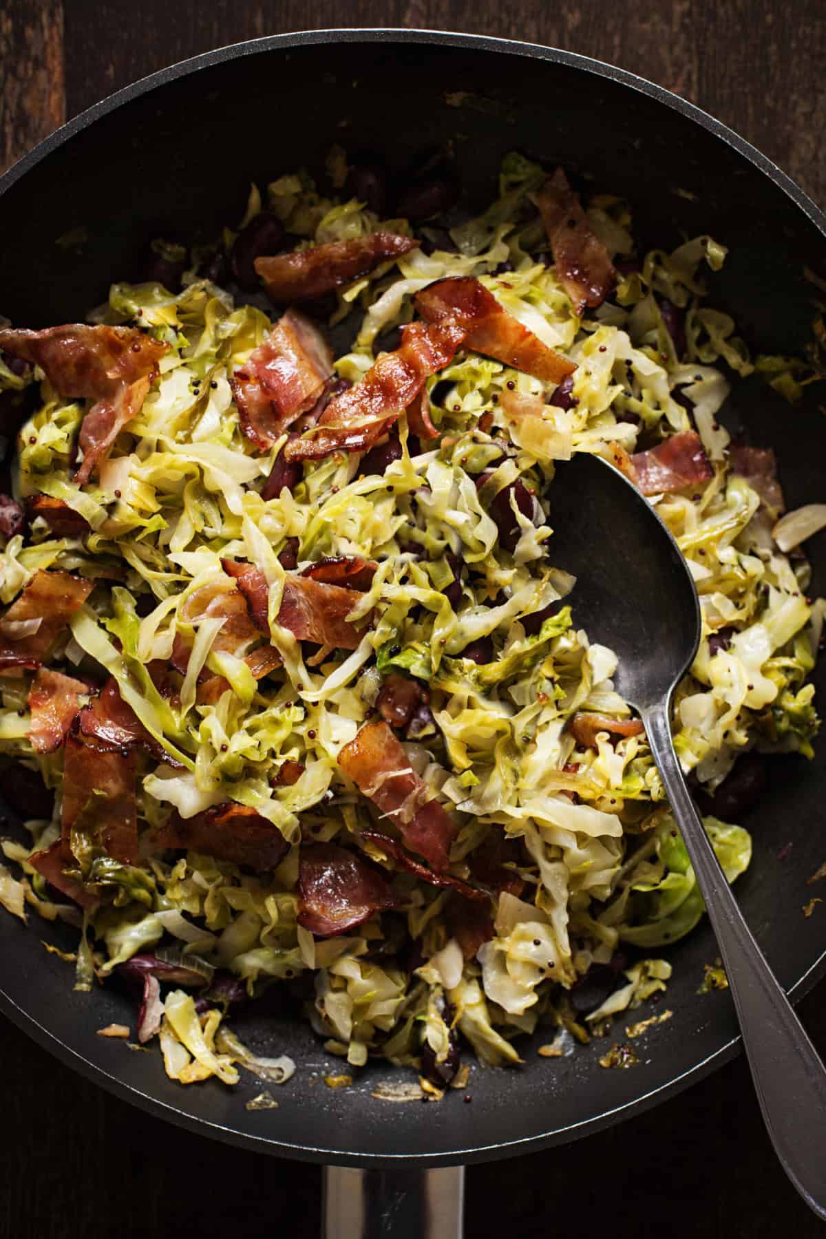 Fried cabbage in a skillet with a black spoon