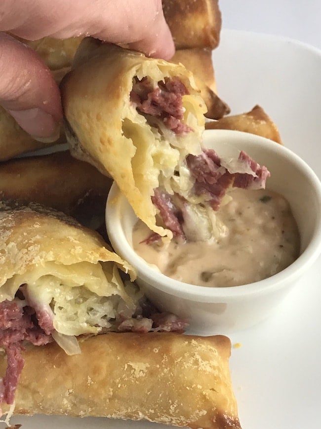 Air Fryer Reuben Egg Rolls being dipped into a sauce