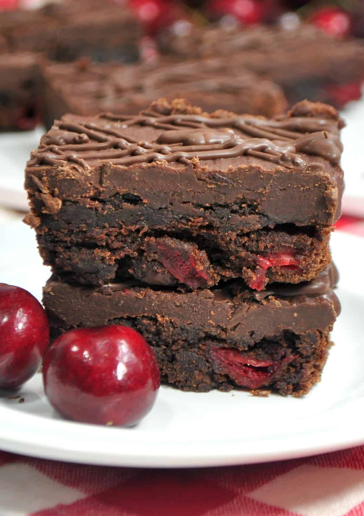 These Black Forest Brownies are rich chocolate brownies combined with cherry pie filling and then topped with a fudgy chocolate ganache! black forest brownies stacked on a plate