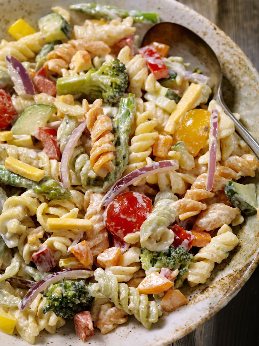 Bowl of pasta with cherry tomatoes, red onion, broccoli florets, and more.