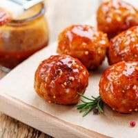 Firecracker Chicken Meatballs on a wooden cutting board next to a basting brush with sauce.