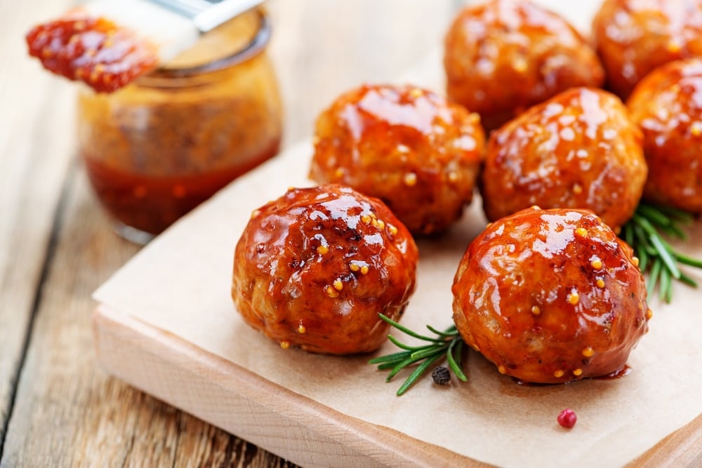 Firecracker Chicken Meatballs on a wooden cutting board next to a basting brush with sauce.