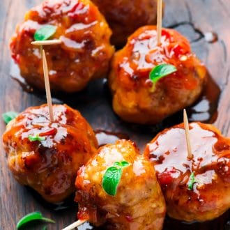 Saucy firecracker chicken meatballs served with toothpicks on a wooden cutting board.