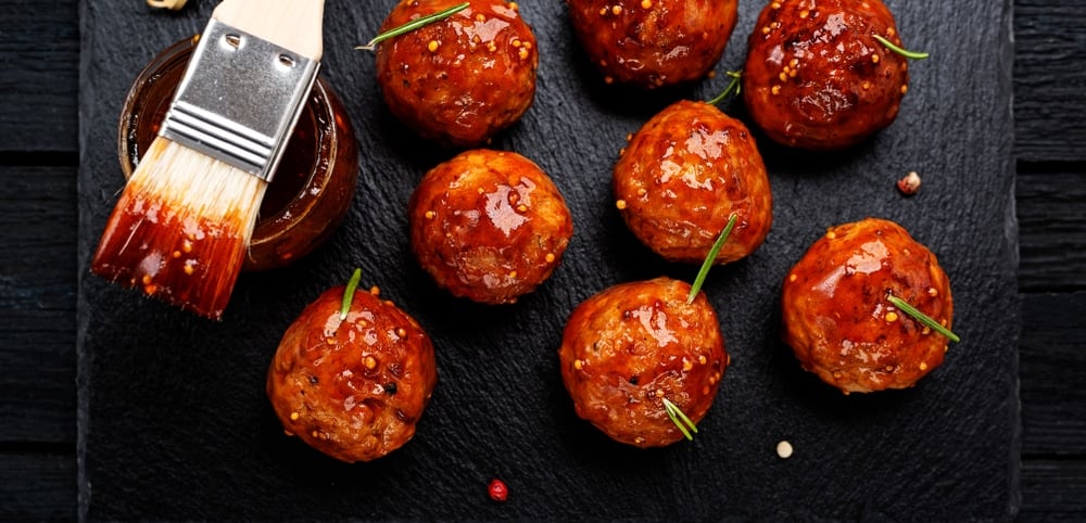Firecracker chicken meatballs glazed with sauce next to a basting brush.