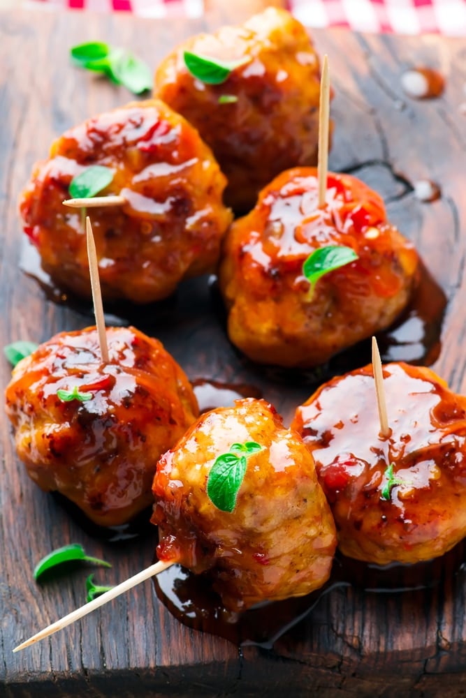 Saucy firecracker chicken meatballs served with toothpicks on a wooden cutting board.