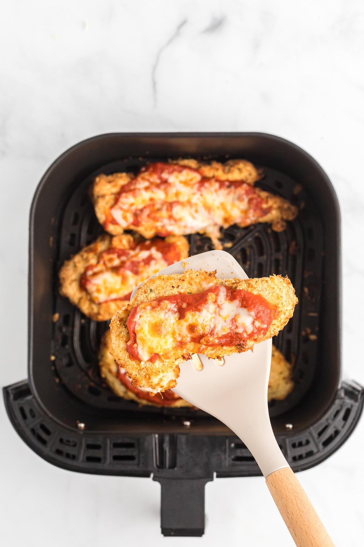 A spatula lifting a chicken parmesan out of the air fryer