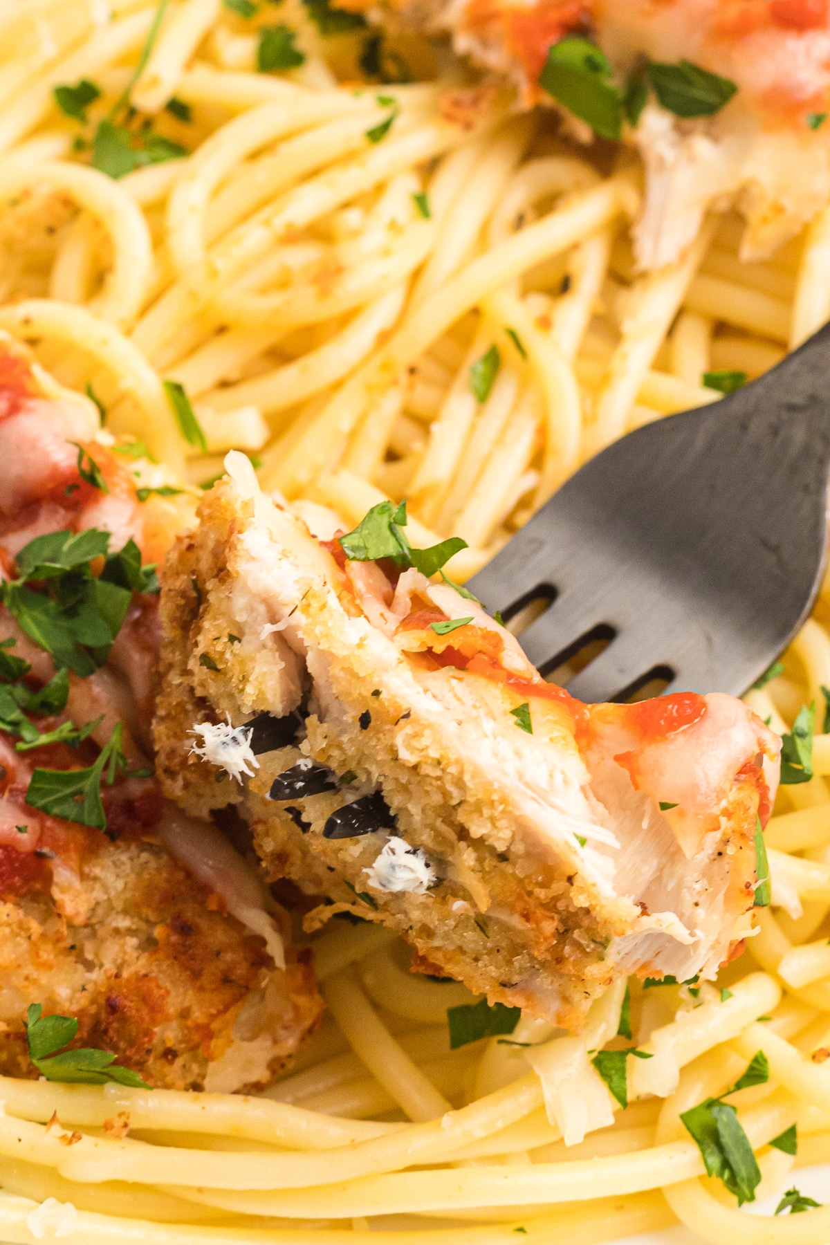 Close-up of a bite of chicken parmesan over pasta