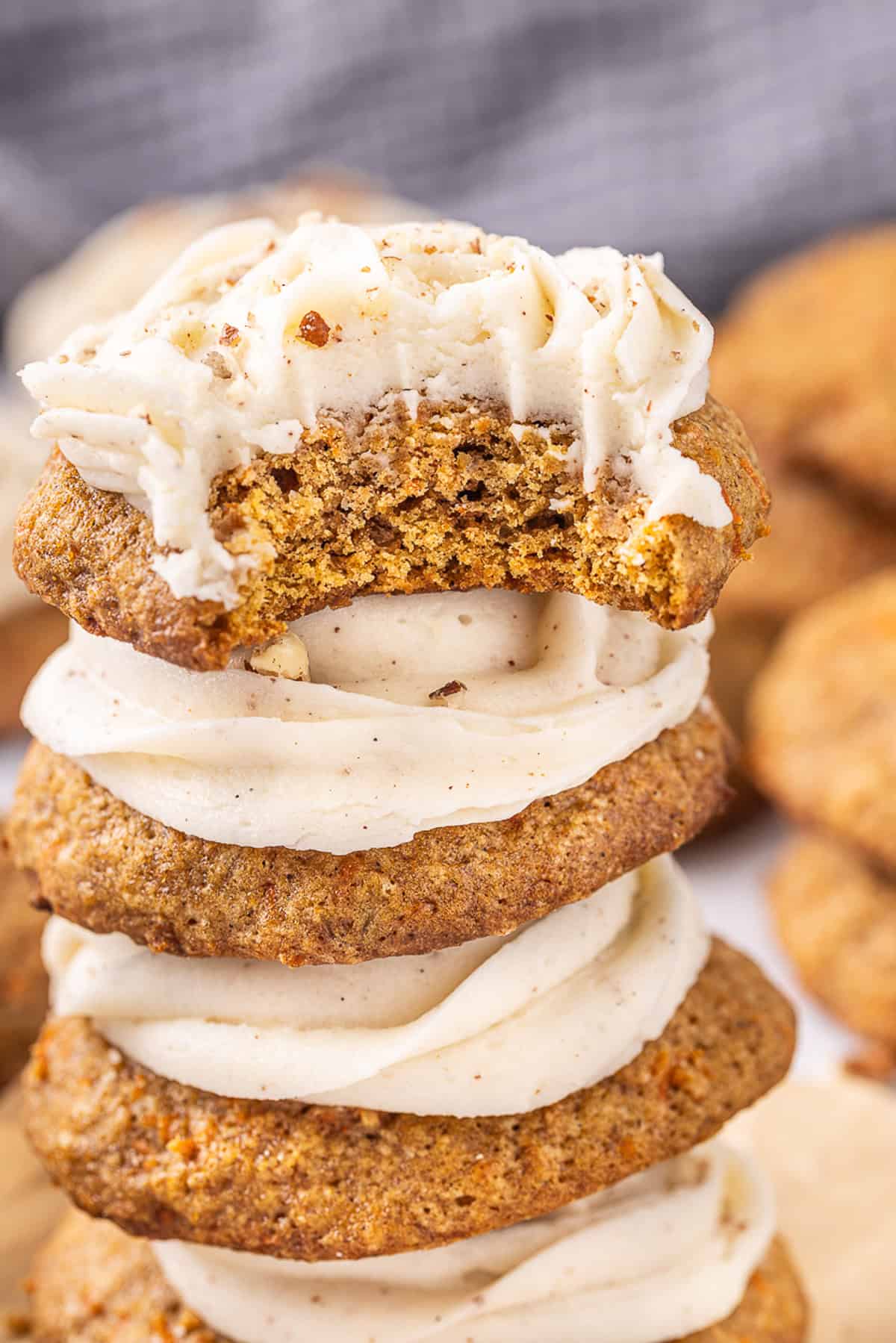 A stack of carrot cake cookies with cream cheese frosting, one with a bite missing