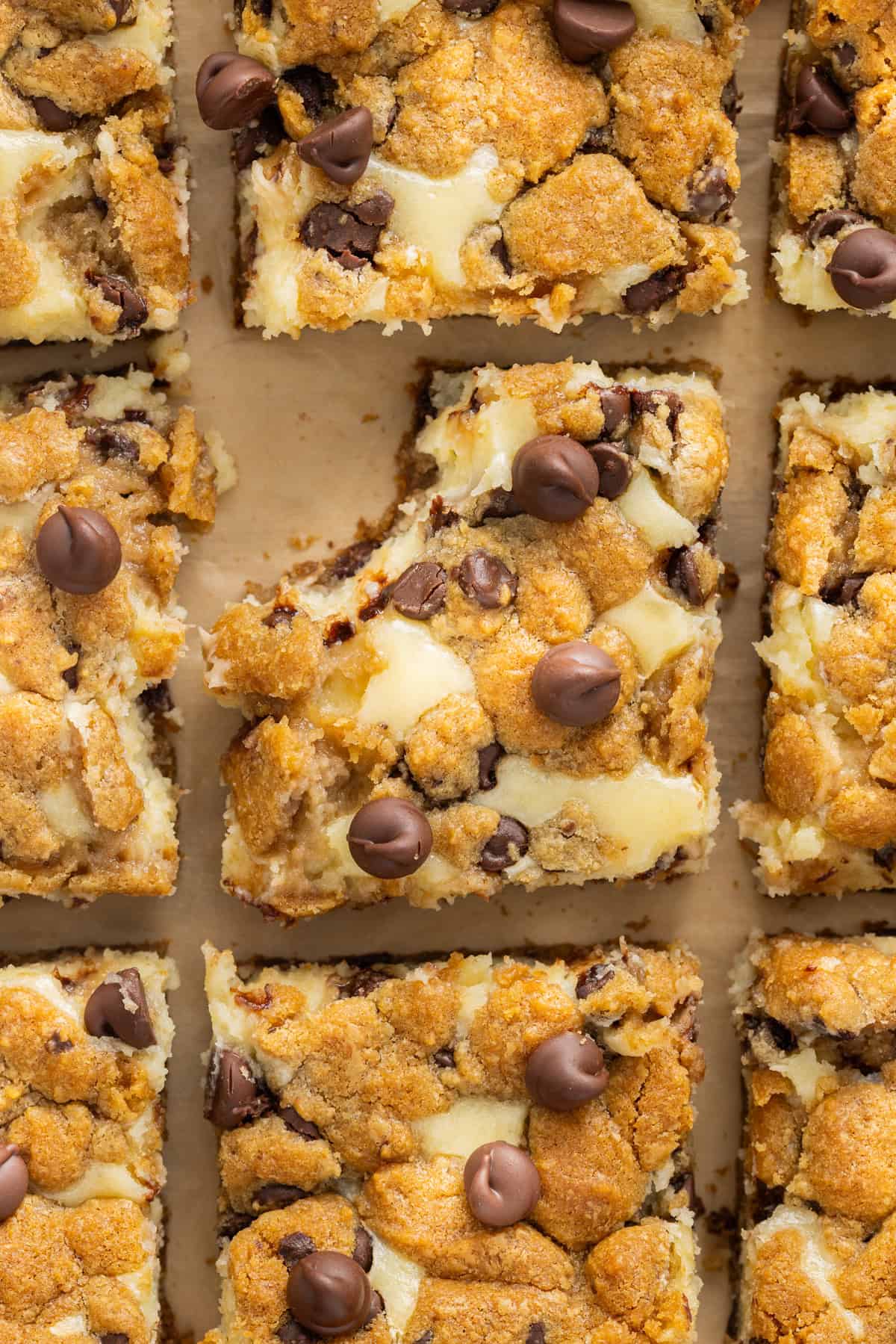 Creamy, tangy cheesecake filling is stuffed between layers of cookie dough in these Chocolate Chip Cheesecake Bars. Overhead view of chocolate chip cheesecake bars, one with a bite missing.