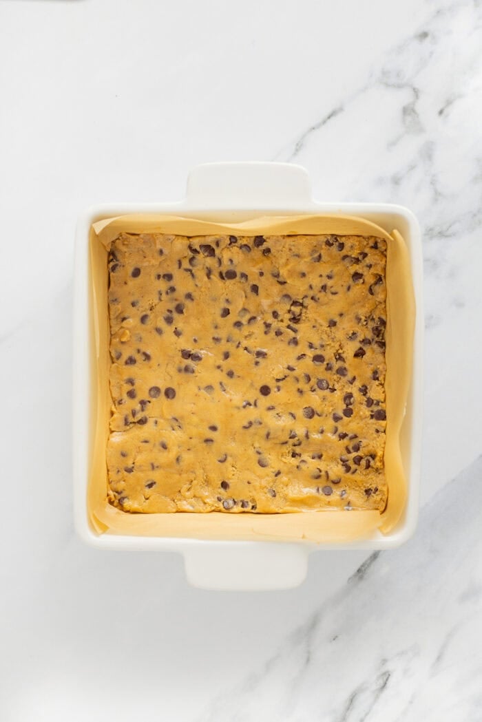 Creamy, tangy cheesecake filling is stuffed between layers of cookie dough in these Chocolate Chip Cheesecake Bars. Chocolate chip cookie dough pressed into a square pan