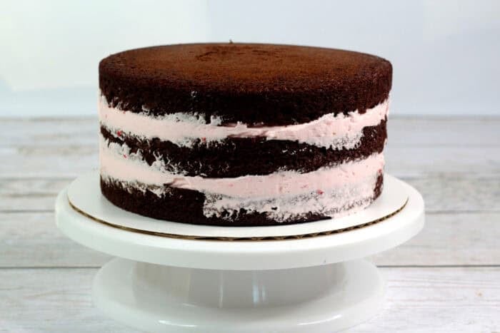 Three chocolate cakes layered with strawberry frosting on a cake stand