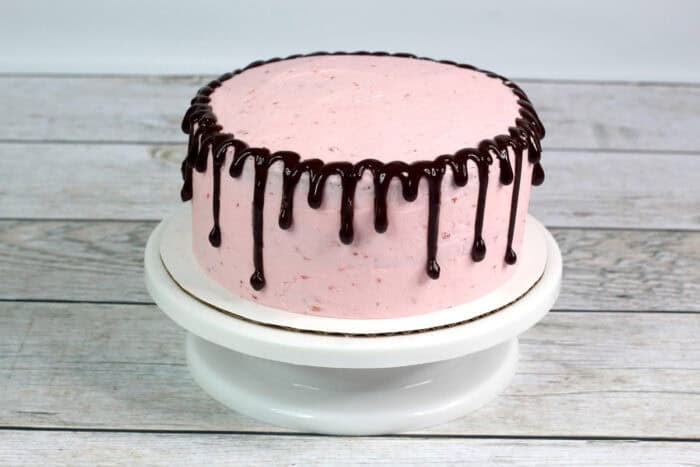 Chocolate ganache dripping down the sides of strawberry frosting on a cake