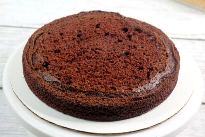 A round chocolate cake with the top removed on a cake stand