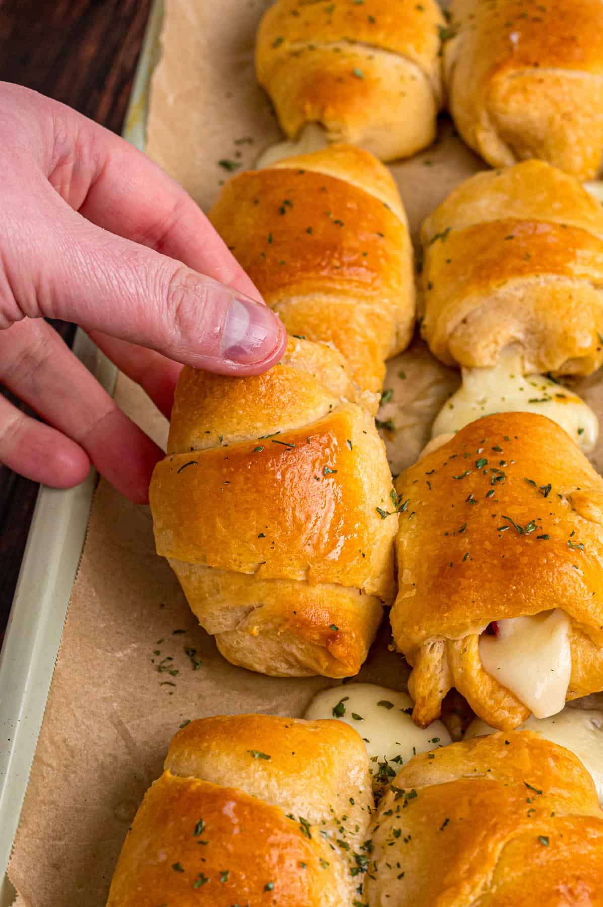 A hand lifting a pizza crescent roll from the baking sheet