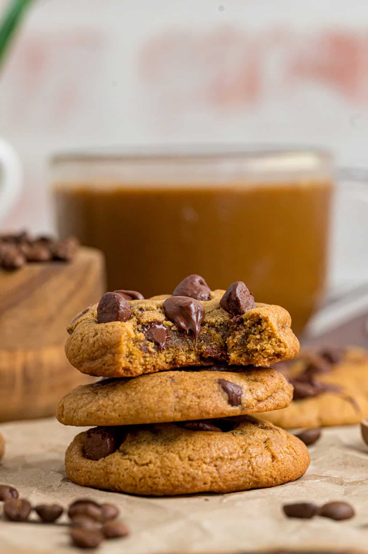 Loaded with chocolate chips and espresso powder, these Coffee Cookies are a coffee lovers dream. A stack of three coffee cookies, one with a bite missing, in front of coffee