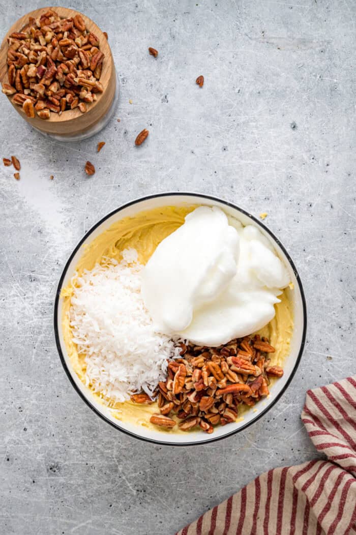 Tender, moist vanilla cake is dotted with coconut and pecans, then topped with cream cheese frosting in this Italian Cream Cake recipe. Egg whites, coconut, and pecans in a bowl of cake batter