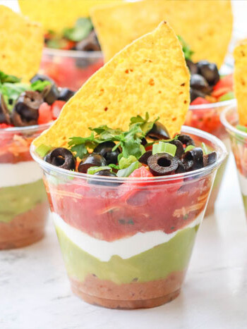 7 layer dip cups with sliced black olives and a tortilla chip on top.