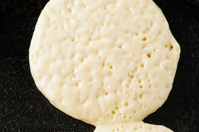 Pancakes on a griddle cooking and ready to flip