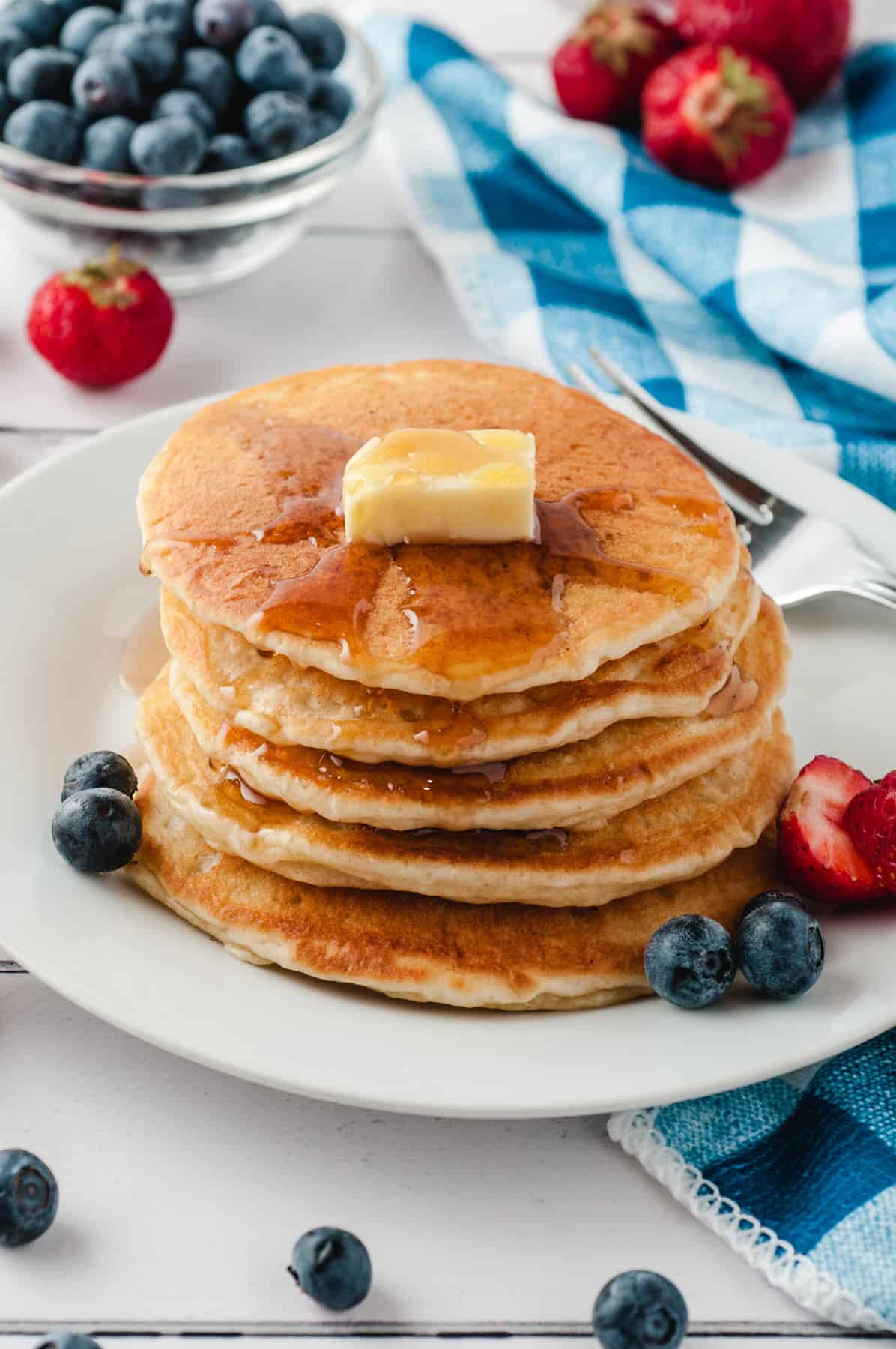 Soft, fluffy, and so flavorful, these Buttermilk Pancakes are made with just 7 basic ingredients in less than 15 minutes. A stack of buttermilk pancakes topped with butter on a white plate