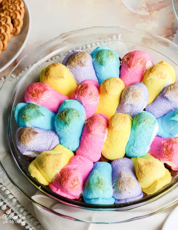 Peep s'mores dip in a round glass baking dish, next to a bowl of cookies.