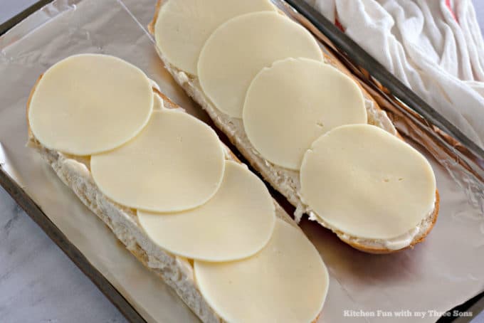 Italian bread topped with mayonnaise and provolone cheese slices