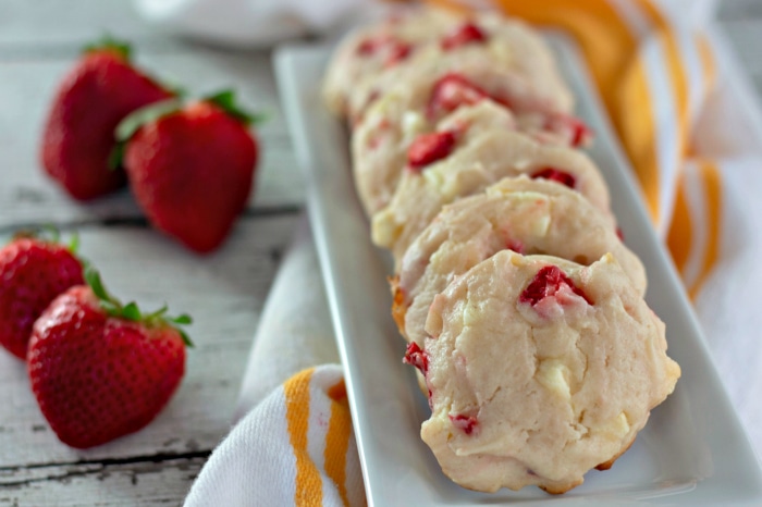 White chocolate strawberry cookies arranged in a row on a narrow platter next to fresh strawberries.