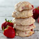 A stack of white chocolate strawberry cookies next to fresh strawberries.