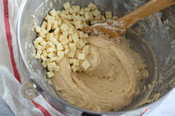 White chocolate chips added to a mixing bowl with cookie dough.